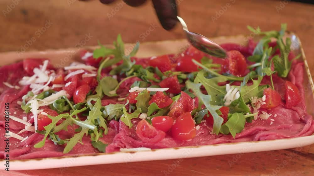 Hands with gloves, adding tomato and cheese flakes on top of fresh red raw meat. Tartare steak carpaccio. Hands with gloves, adding tomato and cheese flakes on top of fresh red raw meat. Tartare steak carpaccio.