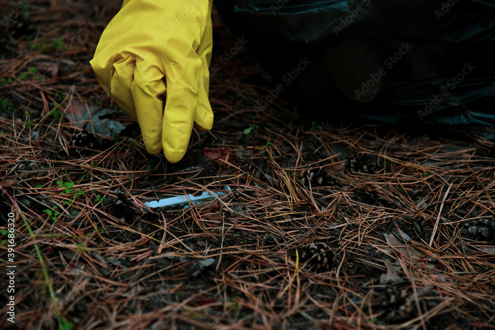 Obraz premium Eco-activist, climate activist, environmental volunteer wearing yellow gloves removes trash into a garbage bag