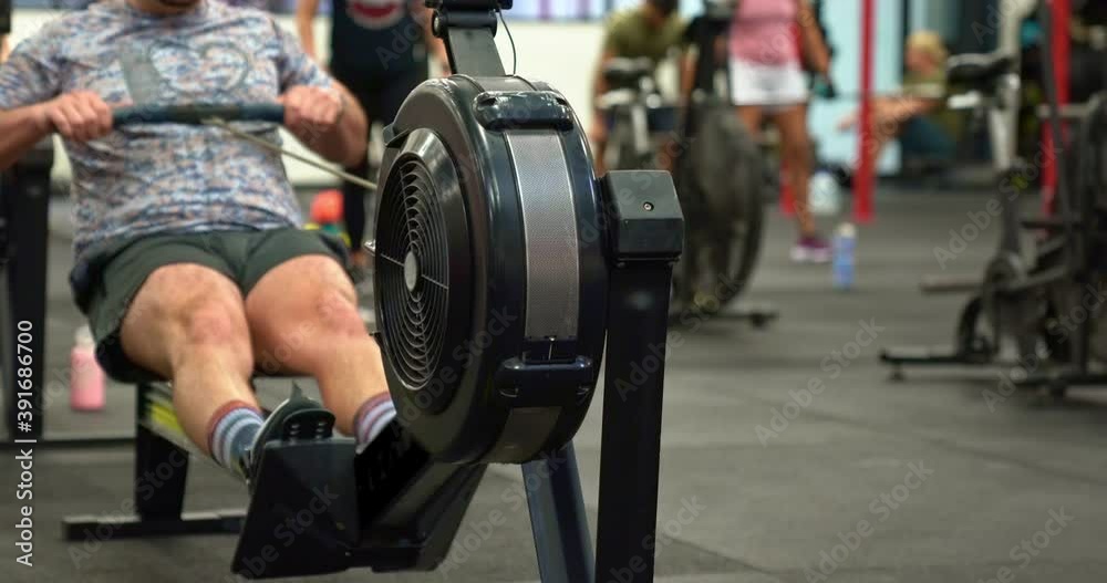 Male athlete on Rowing Machine in busy gym.