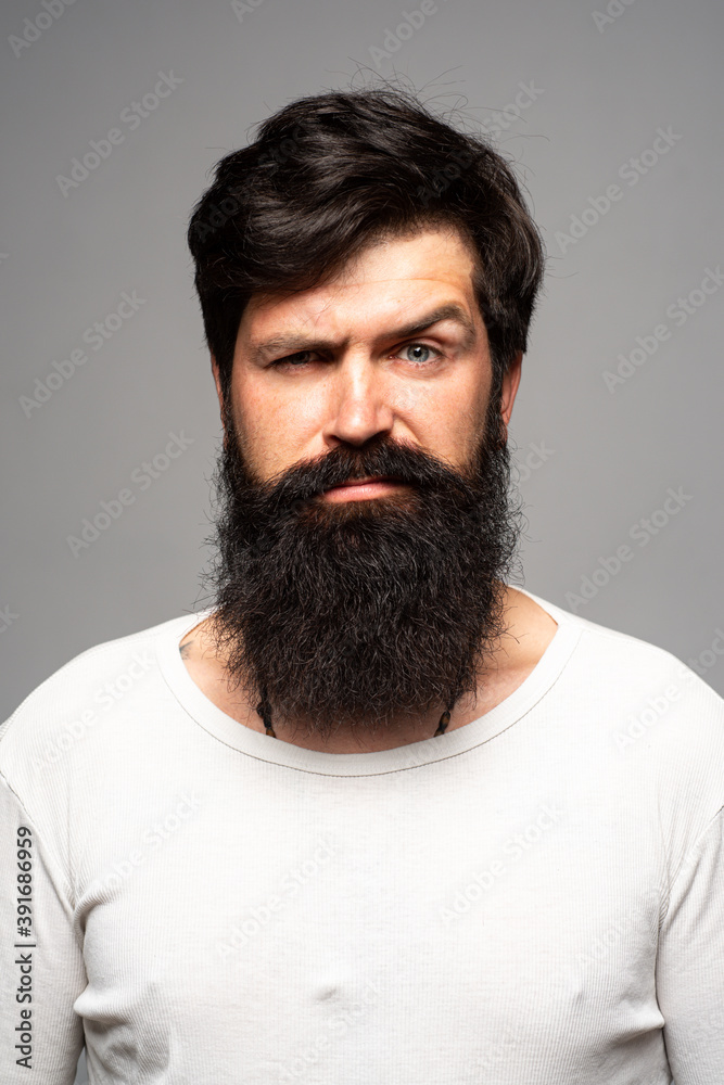 Obraz premium Portrait of confident serious man has beard and mustache, looks seriously, isolated. Hipster guy models in studio. Businessman thinking. Handsome male with beard mustache and trendy hairdo.