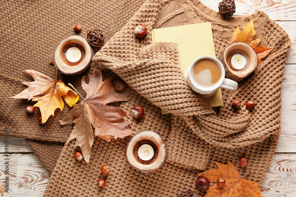 Warm autumn clothes with cup of coffee, candles and book on table Warm autumn clothes with cup of coffee, candles and book on table