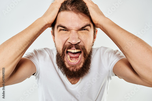 Emotional bearded man in a white t-shirt gestures with his hands light background