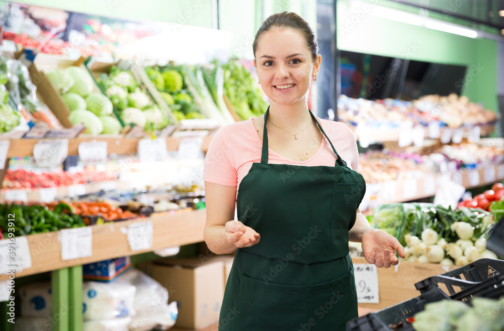 Young smiling saleswoman offering fresh fruits and vegetables in store