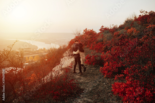 Obraz na płótnie Romantic couple standing and hugging on a autumn hill with beautiful landscape. They watching the sunset. Back view. w salonie