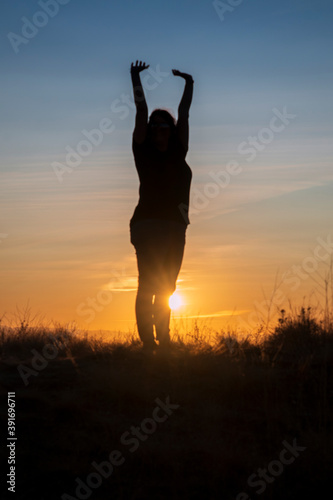 Fototapeta Naklejka Na Ścianę i Meble -  A woman reaches for the sky, stretching in the early morning light.