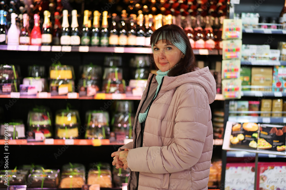 Photo of an adult Caucasian woman on the background of stalls with products in a shopping mall. The model is in outerwear.