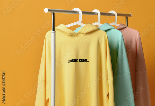 Bilde på lerret Yellow blue and pink hoodies with embroidered text on hangers in the wardrobe clothes shop