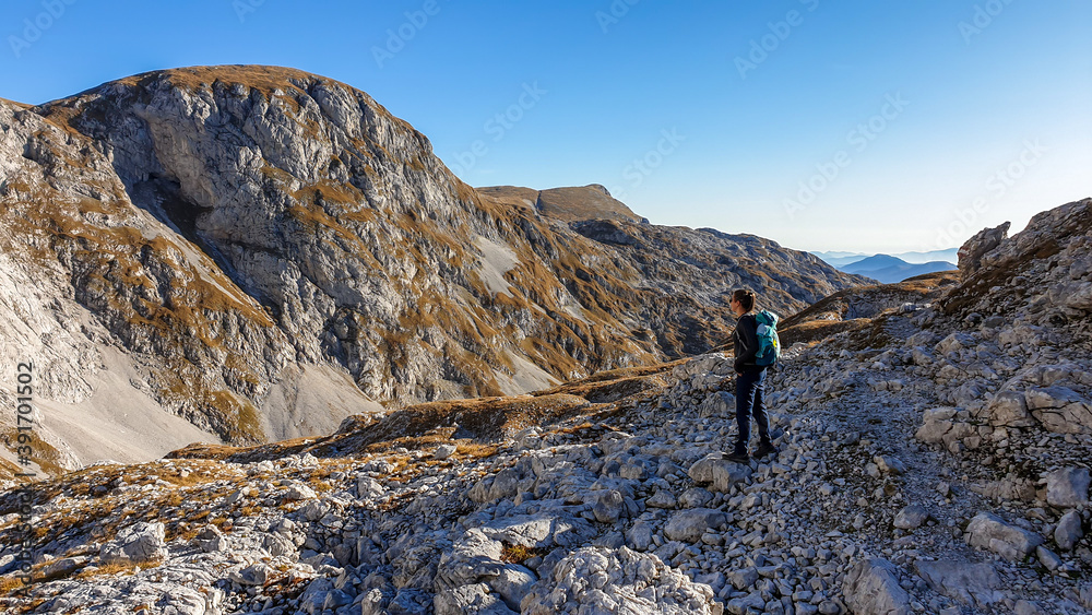 A panoramic capture of a woman hiking in Hochschwab region in Austrian Alps. The flora overgrowing slopes is turning golden. Autumn vibes in the mountains. Idyllic landscape. Freedom and wilderness