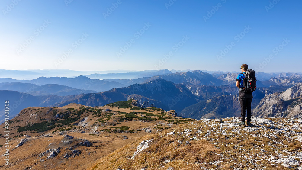 A man with backpack hiking in Hochschwab region in Austrian Alps. The flora overgrowing slopes is golden. Autumn vibes in the mountains. Endless mountain chains shrouded in fog. Freedom and wilderness