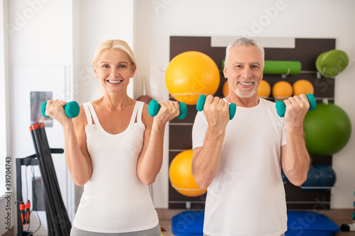Positive man and woman exercising with dumbbells in the gym