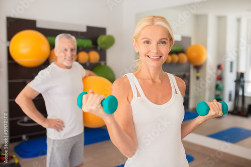 Pretty blonde woman working with dumbbells and smiling