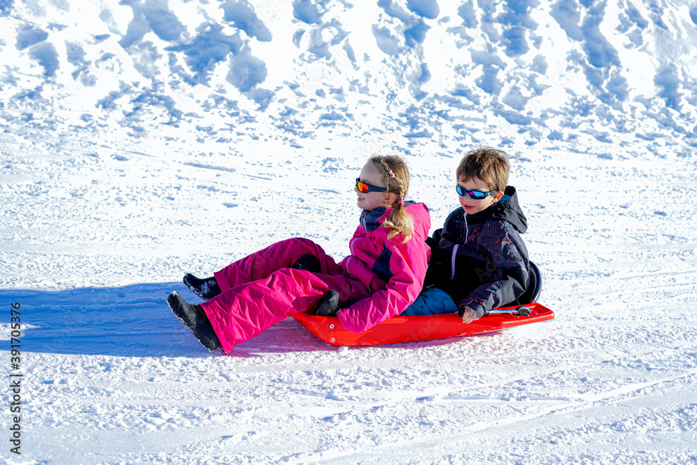 Two joyful kids sledding down the hills on a winter day.