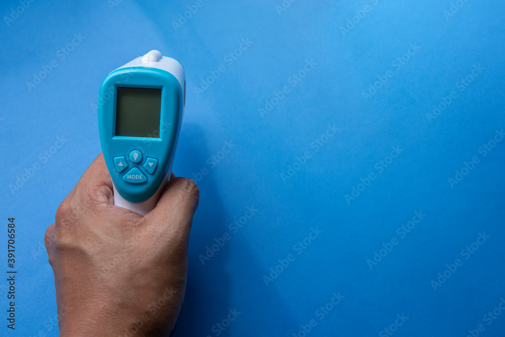 close up of a hand holding a digital infrared thermometer (thermometer gun) isolated on blue background