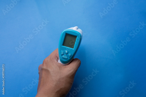 close up of a hand holding a digital infrared thermometer (thermometer gun) isolated on blue background