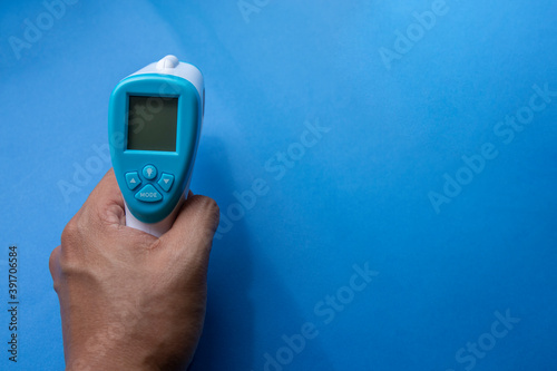 close up of a hand holding a digital infrared thermometer (thermometer gun) isolated on blue background