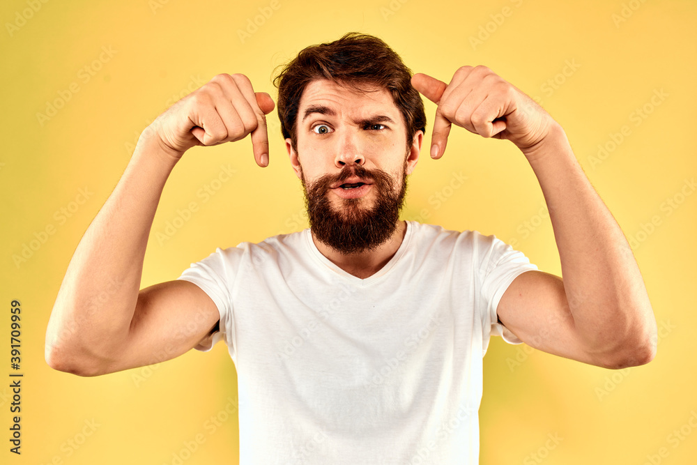 Bearded man emotions fun gesture with hands white t-shirt close-up yellow background Bearded man emotions fun gesture with hands white t-shirt close-up yellow background