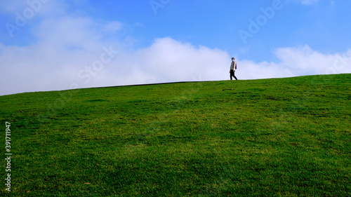 Woman with medical mask walking on a green hillside under blue sky