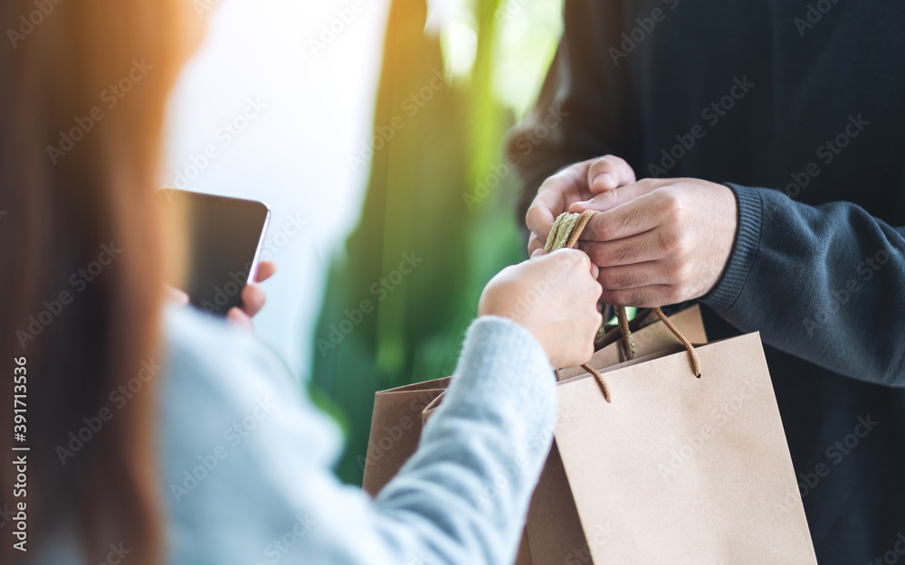 Closeup of a woman holding mobile phone and receiving shopping bags form delivery man