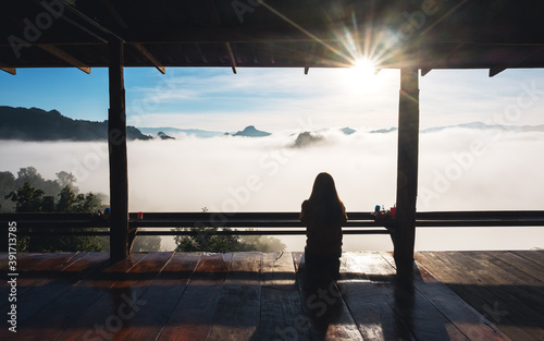 Rear view image of a female traveler sitting and looking at a beautiful sunrise on foggy day