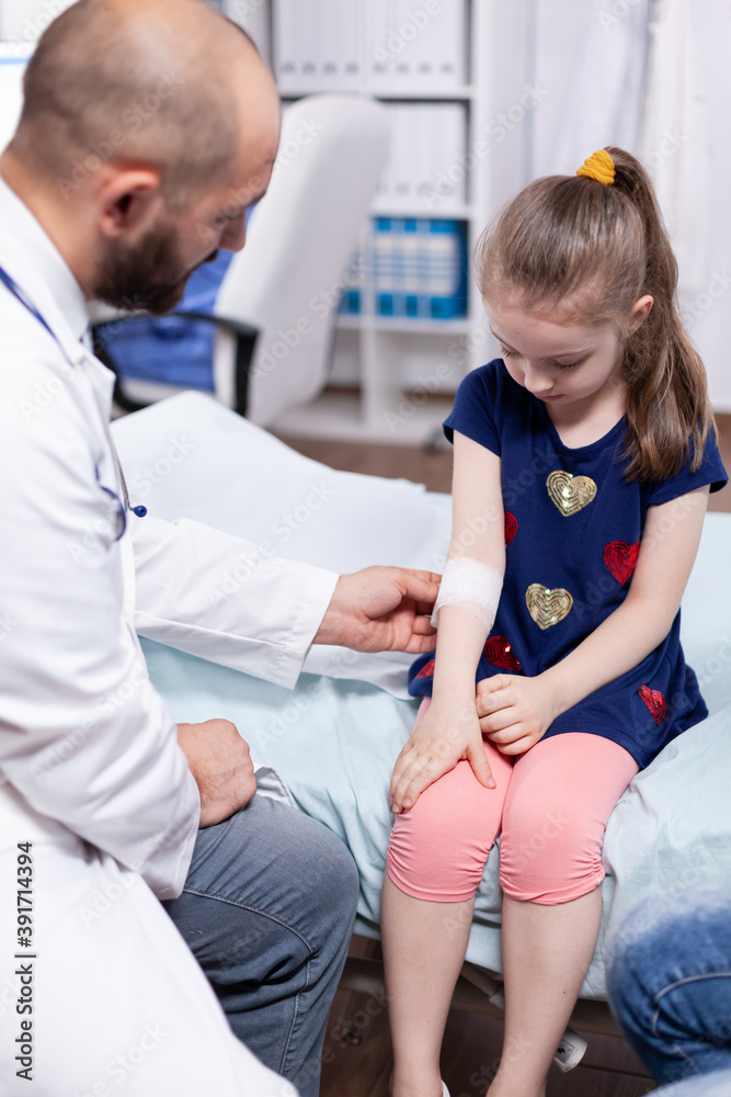 Fototapeta premium Pediatrician bandaging child hand in hospital office during medical examination. Healthcare physician specialist in medicine providing health care services treatment consultation .