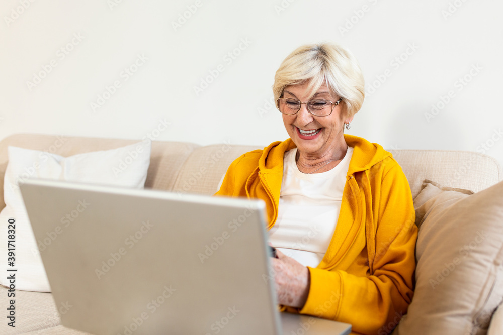 Portrait of senior woman sitting at home on the sofa and working on her laptop. Older lady surfing the net or having video call from home and feeling exiciting. Holding cup of coffee or tea Portrait of senior woman sitting at home on the sofa and working on her laptop. Older lady surfing the net or having video call from home and feeling exiciting. Holding cup of coffee or tea
