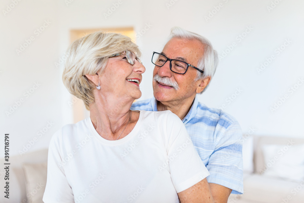 Elderly couple standing in the living room. Portrait of happy senior couple embracing each other in living room at home. Old couple looking each other with love and smilling.