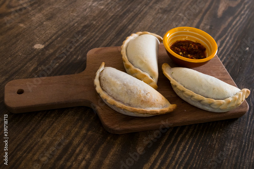 Traditional baked Argentine empanadas savory pastries with meat beef stuffing or vegetables against wooden background and spicy sauce. Latin American fried food