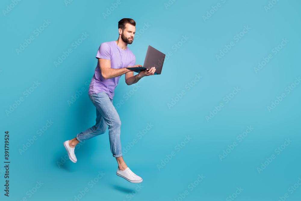 Full length body size photo of focused jumping man typing working on laptop isolated on bright blue color background