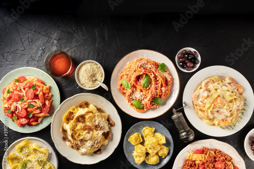 Italian food. Many different pastas, grated Parmesan cheese, ravioli, olives and wine, shot from above on a black background with a place for text