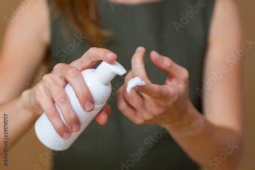 Obraz na płótnie Blonde woman applying a cream on hand with green dress in background. Female pushing moisturizer on fingers from white tube from close up. Young girl pressing container of skin product in detail. w salonie