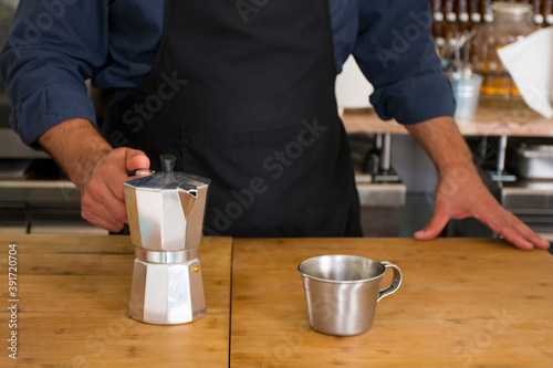Male Barista preparing fresh espresso in coffee maker for customer in a fancy coffee shop. Cafe owner serving a client at the coffee shop