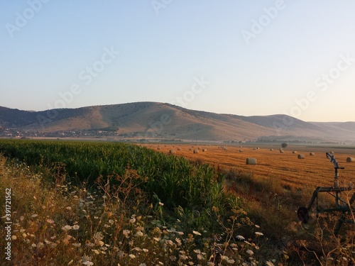 Part of a hose-reel irrigation machine aside. A huge field with straw balls, spread all over a field in background. During the summer, Kozani, Greece.