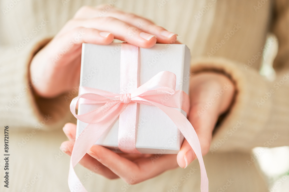 Girl holds in her hands a festive white box with a pink ribbon. A cozy surprise gift for a winter seasonal holiday. Festive lifestyle, hygge. Surprise packaging with decor