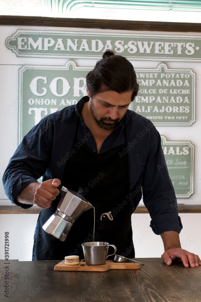 Male Barista preparing fresh espresso in coffee maker for customer in a fancy coffee shop. Cafe owner serving a client at the coffee shop Male Barista preparing fresh espresso in coffee maker for customer in a fancy coffee shop. Cafe owner serving a client at the coffee shop