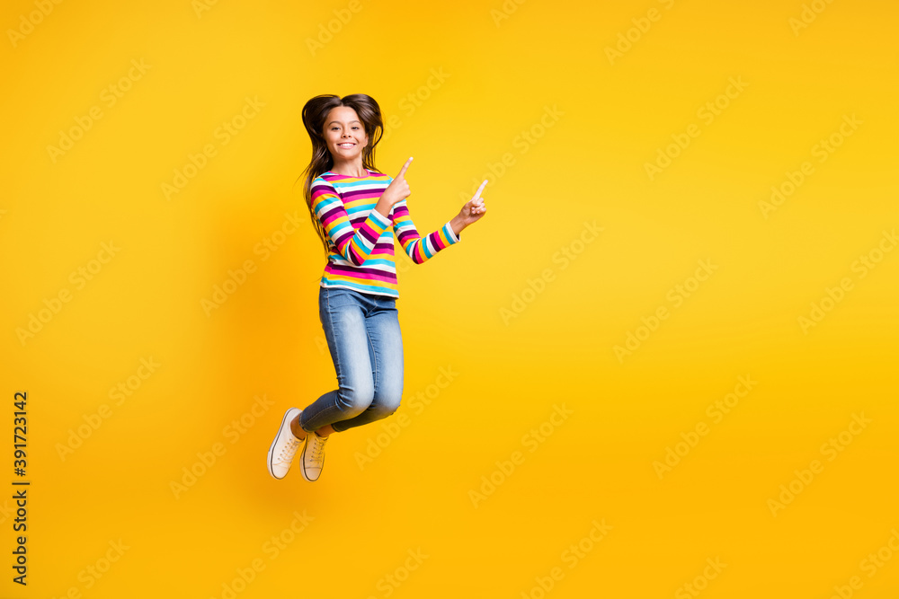 Full length body size photo of jumping high schoolgirl pointing up at empty space isolated on vibrant yellow color background