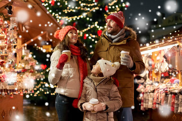 family, winter holidays and celebration concept - happy mother, father and little daughter with takeaway drinks at christmas market on town hall square in tallinn, estonia over snow