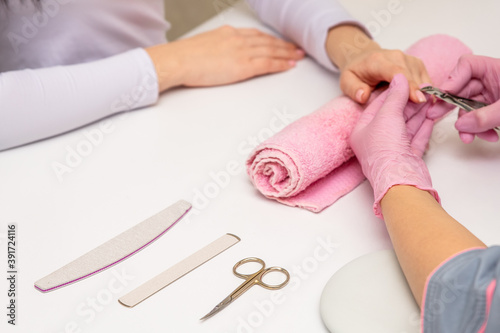 Close-up shot of a manicurist using a cuticle clipper to give a nail manicure to her client in the beauty salon. Master of manicure remove a cuticle nail with nail clipper.