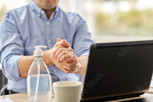 business, health care and pandemic concept - close up of middle-aged man with laptop computer using antibacterial hand sanitizer at home office