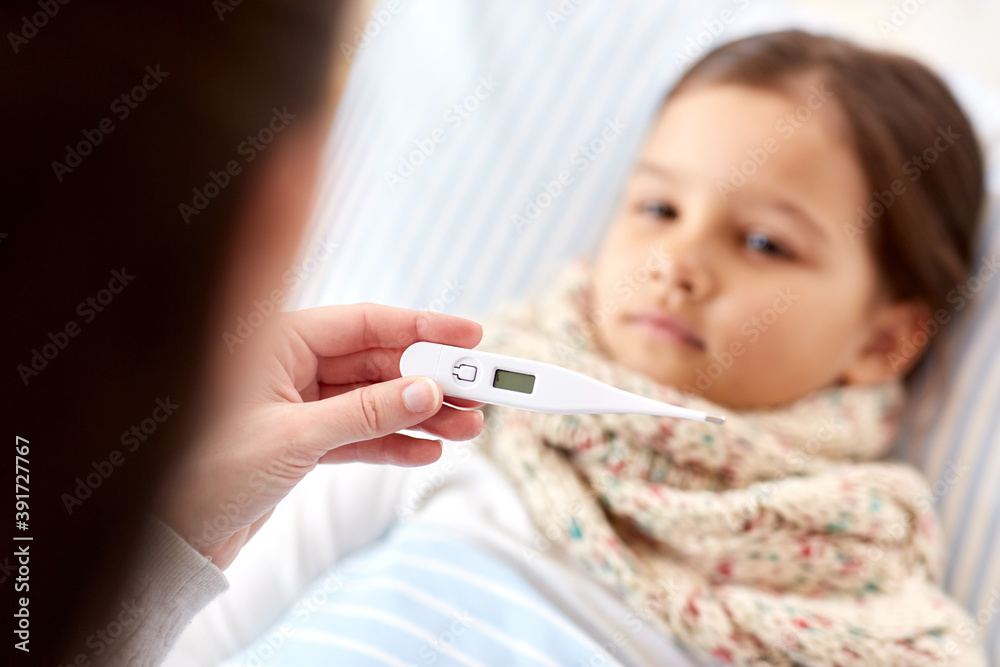 family, health and people concept - mother with thermometer measuring temperature of sick daughter lying in bed at home family, health and people concept - mother with thermometer measuring temperature of sick daughter lying in bed at home