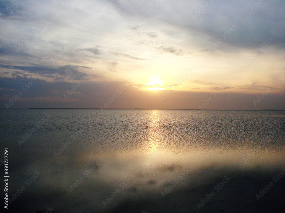 The landscape of the evening sun hides behind the clouds on the horizon, and is reflected by a sunny path on the calm surface of the shallow lake Sivash.