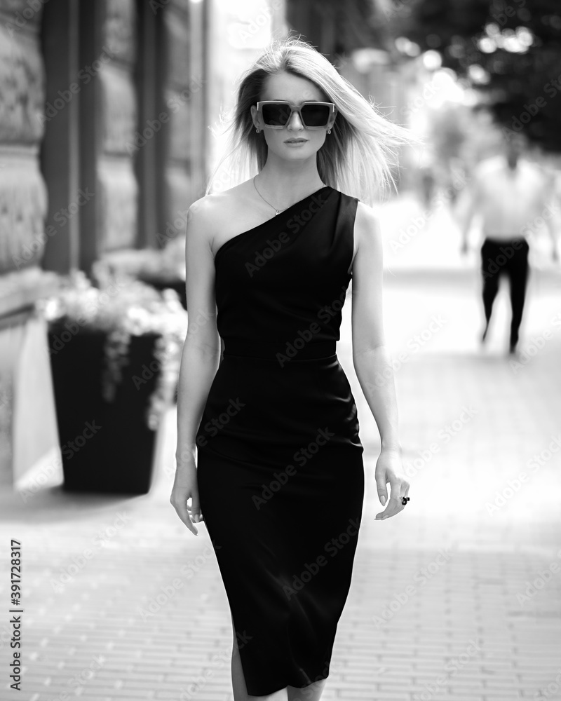 Stylish girl in a black dress walks down the street