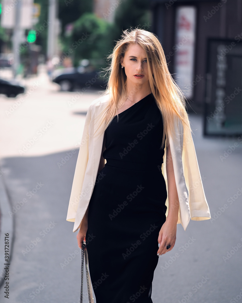 Fashionable girl walks down the street in a black dress and a white jacket Fashionable girl walks down the street in a black dress and a white jacket