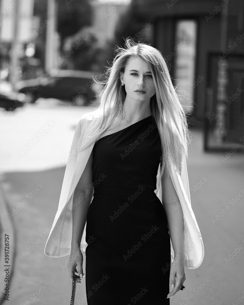 Fashionable girl walks down the street in a black dress and a white jacket
