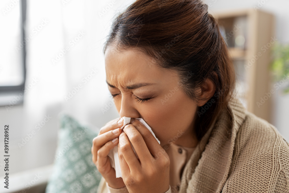 healthcare, cold and people concept - sick asian woman in blanket taking paper tissue from box and blowing her nose at home healthcare, cold and people concept - sick asian woman in blanket taking paper tissue from box and blowing her nose at home
