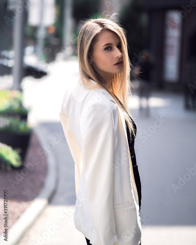 Fashionable girl walks down the street in a black dress and a white jacket
