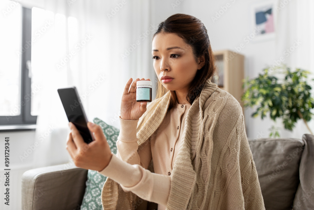 healthcare, technology and people concept - sick asian woman in blanket with medicine having video call on smartphone at home healthcare, technology and people concept - sick asian woman in blanket with medicine having video call on smartphone at home