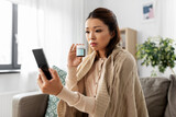 healthcare, technology and people concept - sick asian woman in blanket with medicine having video call on smartphone at home
