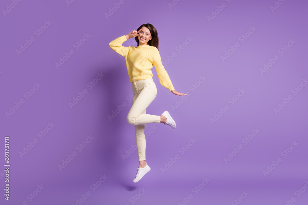 Photo portrait full body view of cheerful girl making v-sign near eye jumping up isolated on bright purple colored background