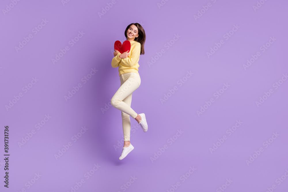 Full length photo portrait of girl hugging heart card jumping up isolated on bright purple colored background