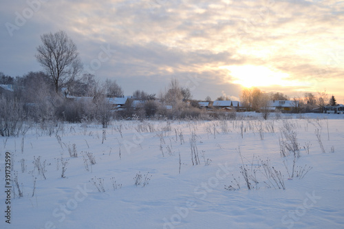 Frosty winter sunrise in the snow-white open spaces near the snow-covered Russian village. Winter nature landscape. © Helena